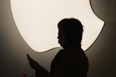 (FILES) This file photo taken on December 23, 2013 shows a woman using her smart phone as she walks past an Apple store in Shanghai.  Arch-rivals Samsung and Apple have decided to drop a series of bitter patent disputes pending in courts outside the United States, the South Korean electronics giant said on August 6, 2014.    AFP PHOTO / FILES / Peter PARKS