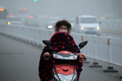 A woman rides a scooter down a polluted street while wearing a face mask in Bozhou, in eastern China's Anhui province on December 24, 2015. Ten Chinese cities were on red alert for smog on December 24, state media reported, as large swathes of the country suffered through their fourth wave of choking pollution this month.     CHINA OUT     AFP PHOTO / AFP / STR