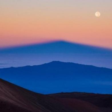  A sombra do vulcão Mauna Kea, no Havaí, é projetada pelo Sol nascente sobre outro vulcão, Hualalai, enquanto a Lua cheia brilha no céu, nesta imagem de Sean Goebel.