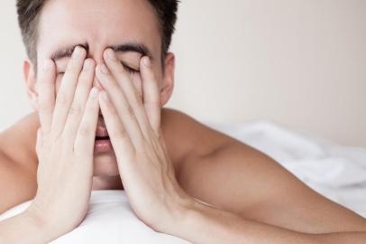 homem cansado na cama com as mãos no rosto