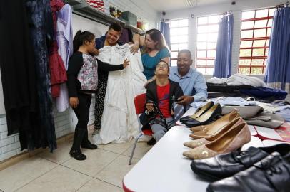 PORTO ALEGRE, RS, BRASIL, 02-10-2017: A aluna especial Anna Luíza de Abreu Moura, a vice-presidente da Associação Comunitária Núcleo Esperança, Débora dos Santos, a professora Gabriela Schneider, o aluno especial Luiz Paulo Decker Soares e o presidente da associação, Pedro Sérgio Corrêa da Silva, observam as doações de trajes para um baile na escola. A Escola Municipal Especial Tristão Sucupira Vianna, no bairro Restinga, precisa de doações para realizar o 3º baile de debutantes para alunos especiais. (Foto: Mateus Bruxel / Agência RBS)