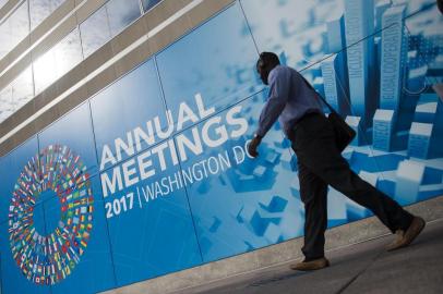 A participant of the 2017 Annual Meetings walks past a sign outside of the International Monetary Fund (IMF) during the 2017 IMF Annual Meetings in Washington, DC, on October 10, 2017. / AFP PHOTO / Andrew CABALLERO-REYNOLDS