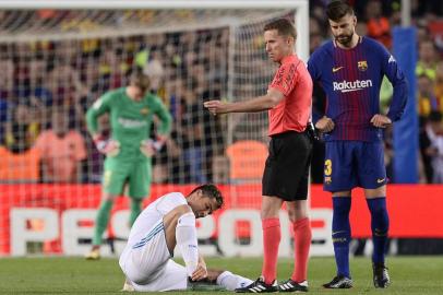 Real Madrids Portuguese forward Cristiano Ronaldo (L) sits on the field after resulting injured dbeside Spanish referee Hernandez Hernandez (C) and Barcelonas Spanish defender Gerard Pique uring the Spanish league football match between FC Barcelona and Real Madrid CF at the Camp Nou stadium in Barcelona on May 6, 2018. / AFP PHOTO / Josep LAGO