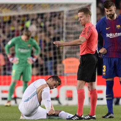 Real Madrids Portuguese forward Cristiano Ronaldo (L) sits on the field after resulting injured dbeside Spanish referee Hernandez Hernandez (C) and Barcelonas Spanish defender Gerard Pique uring the Spanish league football match between FC Barcelona and Real Madrid CF at the Camp Nou stadium in Barcelona on May 6, 2018. / AFP PHOTO / Josep LAGO