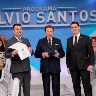 Faustino da Rosa Junior, dono do grupo educacional Facinepe/Inepe, entrega diploma de doutor honoris causa em Comunicação para o comunicador Silvio Santos, dono do canal de televisão SBT, durante programa de auditório do homem do baú. 