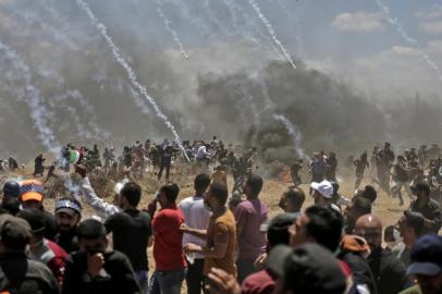  Palestinians run for cover from tear gas during clashes with Israeli forces near the border between the Gaza strip and Israel east of Gaza City on May 14, 2018, as Palestinians protest over the inauguration of the US embassy following its controversial move to Jerusalem.Dozens of Palestinians were killed by Israeli fire on May 14 as tens of thousands protested and clashes erupted along the Gaza border against the US transfer of its embassy to Jerusalem, after months of global outcry, Palestinian anger and exuberant praise from Israelis over President Donald Trumps decision tossing aside decades of precedent. / AFP PHOTO / MAHMUD HAMSEditoria: WARLocal: Gaza CityIndexador: MAHMUD HAMSSecao: demonstrationFonte: AFPFotógrafo: STF