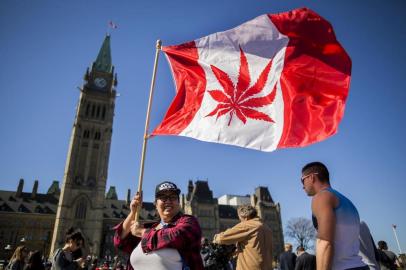 (FILES) In this file photo taken on April 20, 2016 showing a woman waving a flag with a marijuana leef on it next to a group gathered to celebrate National Marijuana Day on Parliament Hill in Ottawa, Canada.Canada lawmakers voted to legalize cannabis on June 18, 2018. / AFP PHOTO / Chris Roussakis