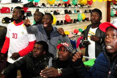  CAXIAS DO SUL, RS, BRASIL, 19/06/2018. Senegaleses se reúnem na loja de Abdoulat Ndiaye, o Billy, presidente da Associação dos Imigrantes Senegaleses, no Centro de Caxias, para assistir Polônia x Senegal, pela Copa do Mundo FIFA 2018. Makhou Laye (com a camisa branca do Senegal) e Serigne Mame Mor Ngom (com a jaqueta do Brasil) estão entre os espectadores. (Diogo Sallaberry/Agência RBS)