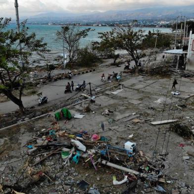 Survivors ride past debris in a devastated area in Palu, Indonesias Central Sulawesi on October 1, 2018, after an earthquake and tsunami hit the area on September 28.Indonesian volunteers began burying bodies in a mass grave with space for more than a thousand people on October 1, victims of a quake-tsunami that devastated swathes of Sulawesi and left authorities struggling to deal with the sheer scale of the disaster. / AFP PHOTO / JEWEL SAMAD