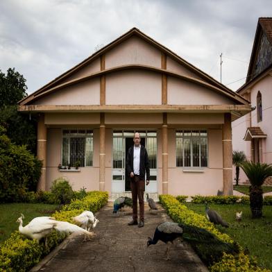  AMETISTA DO SUL. RS, BRASIL, 08/11/2018: Apaixonado por aves exoticas, o padre Gilberto Giacomoni, paroco de Ametista do Sul, cria mais de 20 pavoes soltos no jardim da Paroquia Sao Gabriel, na regiao central da cidade. Os animais, que quando chamados comem na mao do padre, se tornaram atracao turistica no pequeno municipio do extremo norte do RS. (Foto: Mateus Bruxel / Agencia RBS)