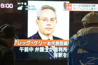 This picture taken on December 21, 2018 shows pedestrians looking at a television news program featuring former former Nissan representative director Greg Kelly in Tokyo. - Japanese authorities suspect former Nissan boss Carlos Ghosn conspired with his right-hand man Kelly to hide away around half of his income (some five billion yen or $44 million) over five fiscal years from 2010. (Photo by Kazuhiro NOGI / AFP)