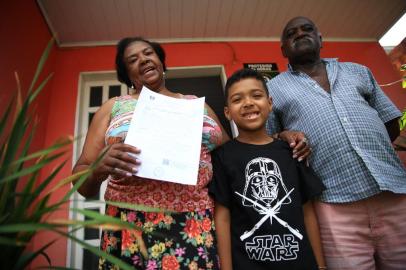  ESTEIO, RS, BRASIL, 27-12-2018. Após processo de regularização, moradores da Vila Pedreira, em Esteio, vão receber certidão de matrícula de imóveis de suas casas. O documento garante que eles possam encaminhar o registro final de seus imóveis. Na foto: Maria Renita Rodrigues, o marido Adão e o neto Eduardo (JEFFERSON BOTEGA/AGÊNCIA RBS)