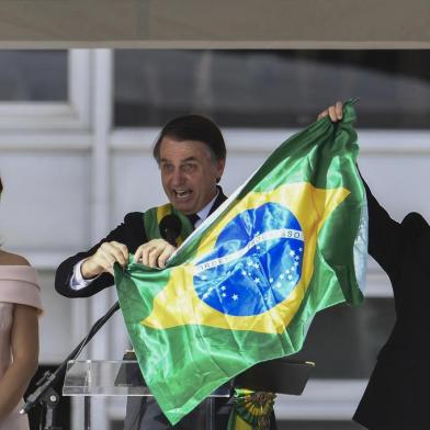  Brazils new President Jair Bolsonaro (C) and Brazils new Vice-President Hamilton Mourao (R), display a Brazilian national flag next to First Lady Michelle Bolsonaro, during their inauguration ceremony at Planalto Palace in Brasilia on January 1, 2019. - Bolsonaro takes office with promises to radically change the path taken by Latin Americas biggest country by trashing decades of centre-left policies. (Photo by EVARISTO SA / various sources / AFP)Editoria: POLLocal: BrasíliaIndexador: EVARISTO SASecao: governmentFonte: EVARISTO SAFotógrafo: STF