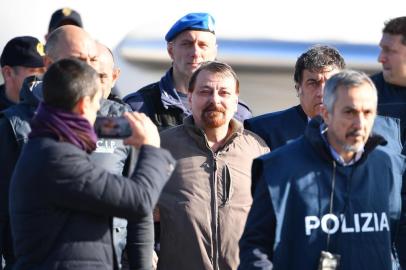  Italian former communist militant Cesare Battisti (C), wanted in Rome for four murders attributed to a far-left group in the 1970s, is escorted by Italian Police officers after stepping off a plane coming from Bolivia and chartered by Italian authorities, after landing at Ciampino airport in Rome on January 14, 2019. - Former communist militant Cesare Battisti landed in Rome on January 14 after an international police squad tracked the Italian down and arrested him in Bolivia, ending almost four decades on the run. (Photo by Alberto PIZZOLI / AFP)Editoria: POLLocal: RomeIndexador: ALBERTO PIZZOLISecao: politics (general)Fonte: AFPFotógrafo: STF