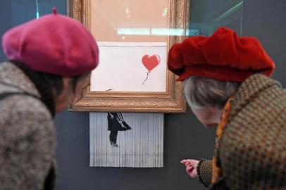 Two women look at the art work Love is in the Bin by British street artist Banksy at the Frieder Burda Museum in Baden-Baden, southwestern Germany, on February 5, 2019. - The art work which was partially destroyed during an auction at Sothebys will be presented in the museum until March 3, 2019. (Photo by Uli Deck / dpa / AFP) / Germany OUT / RESTRICTED TO EDITORIAL USE - MANDATORY MENTION OF THE ARTIST UPON PUBLICATION - TO ILLUSTRATE THE EVENT AS SPECIFIED IN THE CAPTION