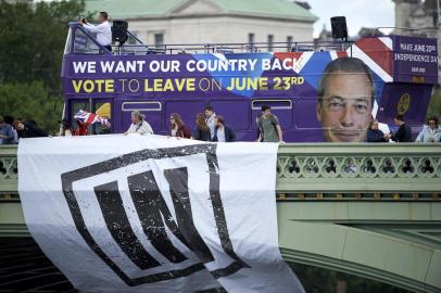 Campaigners to remain in the EU unfurl a banner on Westminster Bridge as a bus bearing the face of UKIP leader Nigel Farage and a message urging voters to leave the EU in the upcoming referendum sits behind it as they wait for a flotilla of boats from the group Fishing for Leave to sail by on the river Thames in London on June 15, 2016.A Brexit flotilla of fishing boats sailed up the River Thames into London today with foghorns sounding, in a protest against EU fishing quotas by the campaign for Britain to leave the European Union. / AFP PHOTO / NIKLAS HALLEN