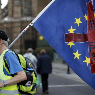 A demonstrator carries a flag as he walks near the Houses of Parliament in central London on March 29, 2019. - British MPs on Friday rejected Prime Minister Theresa May's deal for leaving the European Union for a third time, raising the spectre of a "no deal" exit or a long delay to the process. (Photo by Tolga AKMEN / AFP)