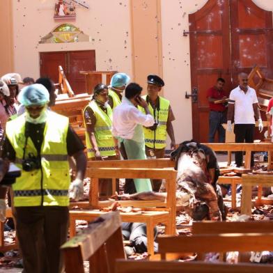 EDITORS NOTE: Graphic content / Sri Lankan security personnel walk past debris next to a dead body slumped over a bench following an explosion in St Sebastians Church in Negombo, north of the capital Colombo, on April 21, 2019. - A series of eight devastating bomb blasts ripped through high-end hotels and churches holding Easter services in Sri Lanka on April 21, killing nearly 160 people, including dozens of foreigners. (Photo by STR / AFP) / GRAPHIC CONTENT