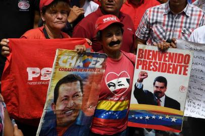 A supporter of Venezuelan President Nicolas Maduro displays placards with pictures of Maduro and late leader Hugo Chavez during a rally on May Day in Caracas on May 1, 2019. - Pro- and anti-government rallies were due to take place in Venezuela, a day after violent clashes erupted in the capital following opposition leader Juan Guido's call on the military to rise up against Maduro, who claimed the insurrection had failed. (Photo by Yuri CORTEZ / AFP)