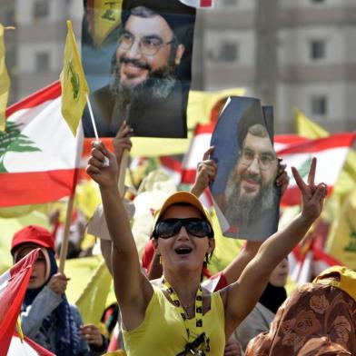 Manifestantes do Hezbollah com bandeiras e fotos do Sheik Hassan Nasrallah em Beirute. NP informações #PÁGINA:26A Hezbollah supporter flashes a Victory-sign and waves a Hezbollah flag, as she shouts slogans during a Hezbollah "Victory over Israel" rally, in Beirut's bombed-out suburbs, Lebanon, Friday, Sept. 22, 2006, as others wave pictures of Hezbollah leader Sheik Hassan Nasrallah. Nasrallah said Friday his guerrilla force would not give up its weapons until Lebanon was "strong," demanding changes in the government as he spoke at a rally of hundreds of thousands of supporters in a defiant challenge to Prime Minister Fuad Saniora. (AP Photo/Hussein Malla) Fonte: AP Fotógrafo: HUSSEIN MALLA