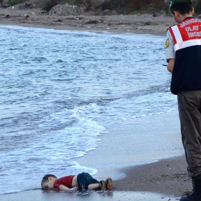 TOPSHOTSGRAPHIC CONTENTA Turkish police officer stands next to a migrant childs dead body off the shores in Bodrum, southern Turkey, on September 2, 2015 after a boat carrying refugees sank while reaching the Greek island of Kos. Thousands of refugees and migrants arrived in Athens on September 2, as Greek ministers held talks on the crisis, with Europe struggling to cope with the huge influx fleeing war and repression in the Middle East and Africa. AFP PHOTO / DOGAN NEWS AGENCY= TURKEY OUT =