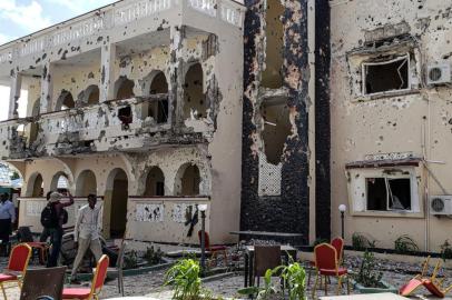 A man passes in front of the rubbles of the popular Medina hotel of Kismayo on July 13, 2019, a day after at least 26 people, including several foreigners, were killed and 56 injured in a suicide bomb and gun attack claimed by Al-Shabaab militants. - A suicide bomber rammed a vehicle loaded with explosives into the Medina hotel in the port town of Kismayo before several heavily armed gunmen forced their way inside, shooting as they went, authorities said. (Photo by STRINGER / AFP)