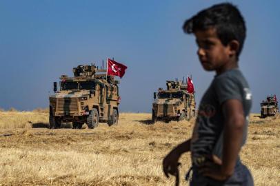 A Syrian boy watches as Turkish military vehicles, part of a US military convoy, take part in joint patrol in the Syrian village of al-Hashisha on the outskirts of Tal Abyad town along the border with Turkey, on October 4, 2019. - The United States and Turkey began joint patrols in northeastern Syria aimed at easing tensions between Ankara and US-backed Kurdish forces. (Photo by Delil SOULEIMAN / AFP)