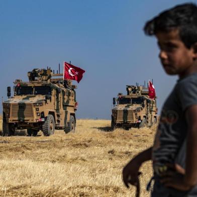 A Syrian boy watches as Turkish military vehicles, part of a US military convoy, take part in joint patrol in the Syrian village of al-Hashisha on the outskirts of Tal Abyad town along the border with Turkey, on October 4, 2019. - The United States and Turkey began joint patrols in northeastern Syria aimed at easing tensions between Ankara and US-backed Kurdish forces. (Photo by Delil SOULEIMAN / AFP)