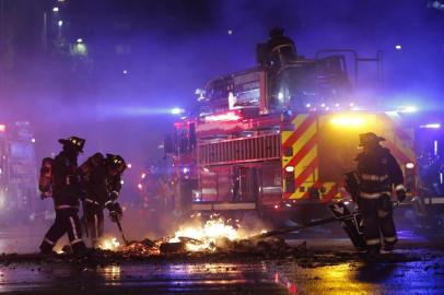 Firefighters extinguish a barricade placed by protesters in downtown Santiago on October 18, 2019, following a mass fare-dodging protest. - The entire Santiago Metro, which mobilizes about three million passengers per day, stopped operating on Friday afternoon following attacks in rejection of the rate hike, the company said. (Photo by JAVIER TORRES / AFP)