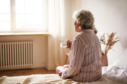 Rear view of senior sixty year old woman with gray hair holding mug washing down sleeping pill, suffering from insomnia. Elderly retired female taking medicine with water, sitting in bedroomPORTO ALEGRE, RS, BRASIL, 22/10/2019- Senhora tomando remédio. (Foto: shurkin_son / stock.adobe.com)Fonte: 284095310