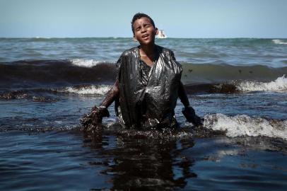 A boy walks out of the sea while removing oil spilled on Itapuama beach located in the city of Cabo de Santo Agostinho, Pernambuco state, Brazil, on October 21, 2019. - Large blobs of oil staining more than 130 beaches in northeastern Brazil began appearing in early September and have now turned up along a 2,000km stretch of the Atlantic coastline. The source of the patches remain a mystery despite President Jair Bolsonaros assertions they came from outside the country and were possibly the work of criminals. (Photo by LEO MALAFAIA / AFP)