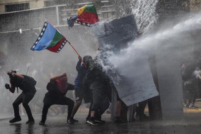 Demonstrators protesting against the economic policies of the government of President Sebastian Pinera are sprayed with a water cannon during clashes with riot police in Santiago, on November 4, 2019. - Unrest began in Chile last October 18 with protests against a rise in transport tickets and other austerity measures and descended into vandalism, looting, and clashes between demonstrators and police. Protesters are angry about low salaries and pensions, poor public healthcare and education, and a yawning gap between rich and poor. (Photo by RODRIGO ARANGUA / AFP)