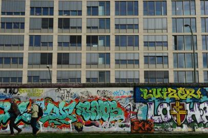  People walk along a grafitti-covered stretch of the Berlin wall, on the west side of the East Side Gallery, a stretch of the Berlin wall, in Berlin on November 3, 2014. This stretch of the Berlin wall, taken over by artists who decorated the yet untouched east side with artwork and political statements after the wall was taken down in 1989-1990, was renovated ahead of the 20th anniversary of the fall of the wall. Though designated as a historical landmark, the paintings have yet again been covered in grafitti. AFP PHOTO / JOHN MACDOUGALLEditoria: ACELocal: BerlinIndexador: JOHN MACDOUGALLSecao: historyFonte: AFPFotógrafo: STF