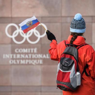 (FILES) In this file photograph taken on December 5, 2017, a supporter waves a Russian flag in front of the logo of the International Olympic Committee (IOC) at their headquarters in Pully near Lausanne. - In Russia, where criticism of the authorities can lead to dire consequences, the head of the countrys anti-doping agency Yury Ganus has openly accused officials of tampering with data handed to the global watchdog. Its dangerous but its my mission, the head of RUSADA told AFP, asked if he felt afraid after assigning blame to the sports ministry and Russian law enforcement. The executive of the World Anti-Doping Agency (WADA) is to meet in Lausanne, Switzerland on December 9, 2019, to decide on a proposed four-year international ban of Russian athletes over the handling of doping allegations. (Photo by Fabrice COFFRINI / AFP)