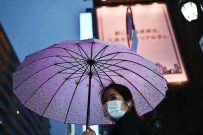 A woman wearing a face mask holds an umbrella as she walks down a street in the rain in Tokyos Ginza area on March 10, 2020. (Photo by CHARLY TRIBALLEAU / AFP)<!-- NICAID(14446347) -->