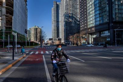 A woman wearing a face mask as a preventive measure against the COVID-19 coronavirus rides a bicycle on a deserted street in the financial district in Beijing on March 3, 2020. - The world has entered uncharted territory in its battle against the deadly coronavirus, the UN health agency warned, as new infections dropped dramatically in China on March 3 but surged abroad with the US death toll rising to six. (Photo by NICOLAS ASFOURI / AFP)<!-- NICAID(14438757) -->