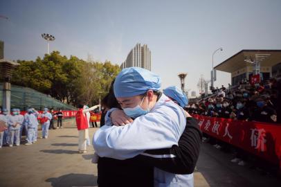 Médico (à direita) abraça um membro de uma equipe de assistência médica da província de Jiangsu em uma cerimônia que marca sua partida após ajudar no esforço de recuperação de coronavírus em Wuhan, na província central de Hubei, na China, em 19 de março de 2020.Equipes médicas de toda a China começaram a deixar Wuhan esta semana depois que o número de novas infecções por coronavírus diminuiu.Em 19 de março, a China não registrou novos casos domésticos de coronavírus pela primeira vez desde que começou a registrá-los em janeiro, mas registrou um aumento nas infecções do exterior.A medical worker (R) embraces a member of a medical assistance team from Jiangsu province at a ceremony marking their departure after helping with the COVID-19 coronavirus recovery effort, in Wuhan, in Chinas central Hubei province on March 19, 2020. - Medical teams from across China began leaving Wuhan this week after the number of new coronavirus infections dropped. China on March 19 reported no new domestic cases of the coronavirus for the first time since it started recording them in January, but recorded a spike in infections from abroad. (Photo by STR / AFP) / China OUT<!-- NICAID(14455875) -->