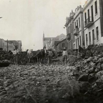 Rua Sinimbu, entre a Garibaldi e a Visconde de Pelotas, antes e depois das obras de rebaixamento, em 1940. Vê-se à esquerda, o prédio da antiga sede do Recreio da Juventude (posterior Farmácia do Círculo Operário Caxiense) e, na quadra seguinte, o prédio dos Correios, a antiga Casa Mandelli e, em frente, a Casa Bragagnolo. Ao fundo, à direita, a Casa Magnabosco e a Catedral Diocesana. À direita, em primeiro plano, a residência de João e Anna Mattana e, ao lado, a sede da Associação Rural de Caxias. Na esquina, o extinto prédio da loja Irmãos Calcagnotto, posteriormente Armarinhos Caxias e atualmente Casa & Cia. Mais acima também localizava-se a lendária Funerária Curtolo e, na esquina, a casa da família Serafini (em frente ao Magnabosco).<!-- NICAID(14463873) -->