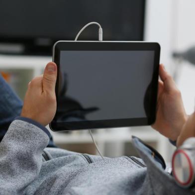 Male hand holds tablet in home setting whilePORTO ALEGRE, RS, BRASIL, Quatro em cada cinco adolescentes são sedentários. (Foto: ¿¿¿¿ ¿¿¿¿¿¿¿¿ / stock.adobe.com)Fonte: 303669977<!-- NICAID(14334042) -->