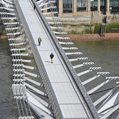 Pedestrians cross a quiet Millennium Footbridge across the River Thames in London in the mid-morning on March 17, 2020 after the UK government announced stricter measures and social distancing advice to deal with the novel coronavirus outbreak. - Britain on Tuesday ramped up its response to the escalating coronavirus outbreak after the government imposed unprecedented peacetime measures prompted by scientific advice that infections and deaths would spiral without drastic action. More firms sent staff to work from home and public transport emptied after the government called for an end to non-essential social contact and unnecessary travel as confirmed COVID-19 cases climbed to more than 1,500 and deaths rose to 55. (Photo by JUSTIN TALLIS / AFP)<!-- NICAID(14454762) -->