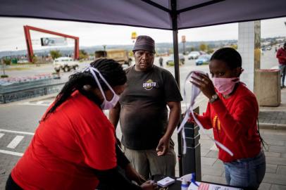  A mall clerk hands out a reusable face mask to a customer to put on at the entrance of a shopping mall in Alexandra, Johannesburg, on April 10, 2020. - Alexandra township local workshop Hluvuku Designs transitioned its production from traditional textiles to reusable face masks to be distributed to its residents at the local mall to help curb the spread of the COVID-19 coronavirus. (Photo by Michele Spatari / AFP)Editoria: HTHLocal: AlexandraIndexador: MICHELE SPATARISecao: diseaseFonte: AFPFotógrafo: STR<!-- NICAID(14476933) -->