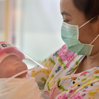 This photo taken through a glass window at a maternity ward shows a nurse holding a newborn baby wearing a face shield, in an effort to halt the spread of the COVID-19 coronavirus, at Praram 9 Hospital in Bangkok on April 9, 2020. (Photo by Lillian SUWANRUMPHA / AFP)<!-- NICAID(14477029) -->