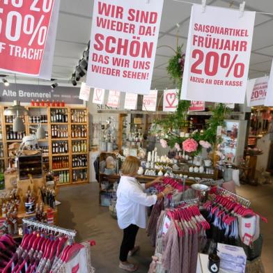 A banner reading We are back! Nice to see you again hangs in a shop as a woman looks at clothes in Ludwigsburg on April 20, 2020. - Germany  starts easing its lockdown restrictions from April 20, 2020 and allows the re-opening of shops with a maximum sales area of up to 800 square meters. (Photo by THOMAS KIENZLE / AFP)<!-- NICAID(14481855) -->