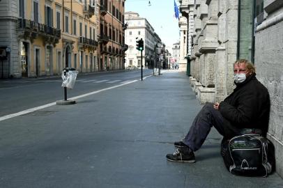 A homeless man sits in a deserted Via del Corso main street in central Rome on March 24, 2020 during the countrys lockdown aimed at stopping the spread of the COVID-19 (new coronavirus) pandemic. (Photo by Vincenzo PINTO / AFP)<!-- NICAID(14460223) -->