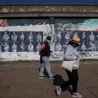 A couple walks past a wall displaying pictures of Uruguayan outstanding figures posing with portraits of people disappeared during the military dictatorship (1973-1985), in Montevideo on May 18, 2020. - Next May 20 marks the 25th anniversary of the so-called Marcha del Silencio (March of Silence), held each year to commemorate the murder of Uruguayan congressmen Zelmar Michelini and Hector Gutierrez Ruiz -killed by a military commando while in exile in Argentina during the plan Condor period- and to demand justice in the unsolved cases of missing people. Due to restrictions on the COVID-19 pandemic, this years rally will be held virtually, through several activities within social media. (Photo by Eitan ABRAMOVICH / AFP)<!-- NICAID(14504004) -->