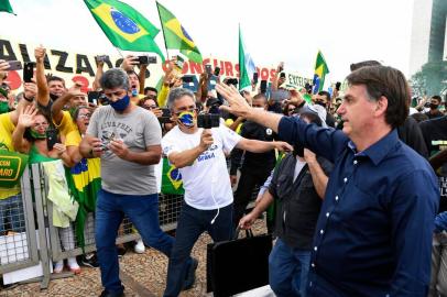 Brazils President Jair Bolsonaro greets supporters upon arrival at Planalto Palace in Brasilia, on May 24, 2020, amid the COVID-19 coronavirus pandemic. - Despite positive signs elsewhere, the disease continued its surge in large parts of South America, with the death toll in Brazil passing 22,000 and infections topping 347,000, the worlds second-highest caseload. (Photo by EVARISTO SA / AFP)<!-- NICAID(14506800) -->