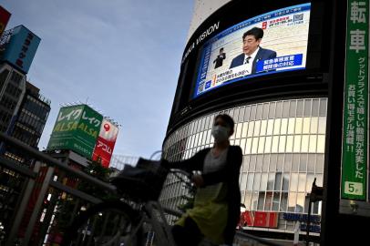 Japans Prime Minister Shinzo Abe (top R) is seen on a live TV broadcast as he announces the lifting of a nationwide state of emergency, as a woman on a bicyle crosses the road in Tokyos Shinjuku area on May 25, 2020. - Japan Prime Minister Shinzo Abe on May 25 lifted the state of emergency imposed nationally to combat coronavirus following a sharp decline in the number of new cases. (Photo by CHARLY TRIBALLEAU / AFP)<!-- NICAID(14507199) -->