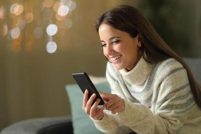  Happy woman in winter using mobile phone in the night sitting on a couch in the living room at homeFonte: 307475303<!-- NICAID(14437256) -->