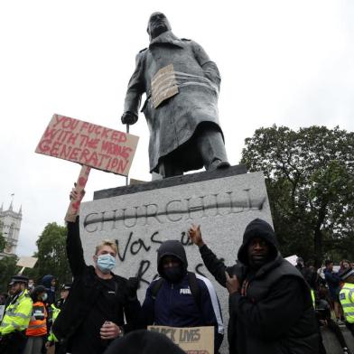 Protesters pose for a photograph in front of the defaced statue of former British prime minister Winston Churchill, with the words (Churchill) was a racist written on its base in Parliament Square, central London after a demonstration outside the US Embassy, on June 7, 2020, organised to show solidarity with the Black Lives Matter movement in the wake of the killing of George Floyd, an unarmed black man who died after a police officer knelt on his neck in Minneapolis. - Taking a knee, banging drums and ignoring social distancing measures, outraged protesters from Sydney to London on Saturday kicked off a weekend of global rallies against racism and police brutality. (Photo by ISABEL INFANTES / AFP)<!-- NICAID(14517461) -->