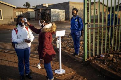 A pupil at the Winnie Mandela Secondary School looks at a teacher taking the temperature of another pupil as she waits in line outside the school premises before classes resume in the Tembisa township, Ekurhuleni, on June 8, 2020. - Grade 7 and grade 12 pupils in South Africa began returning to classrooms on June 8, 2020  after two and a half months of home-schooling to limit the spread of the COVID-19 coronavirus. (Photo by Michele Spatari / AFP)